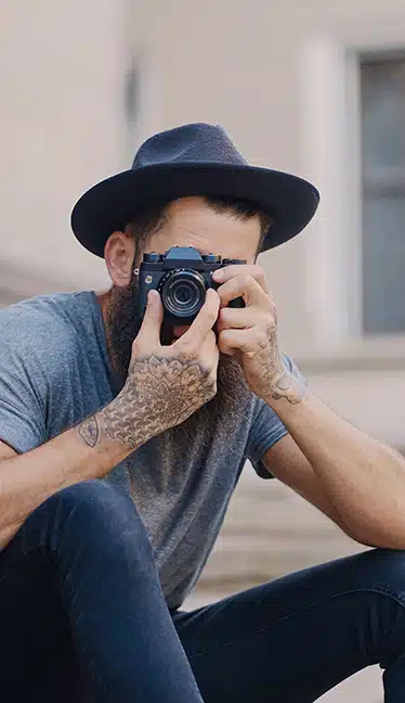 persona con sombrero mirando al frente con una cámara de fotos preparada para fotografiar curso fotografía