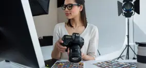 persona con gafas con una cámara en sus manos mirando la pantalla de un ordenador