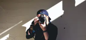 persona con gorra con una cámara en sus manos, preparado para sacar una fotografía