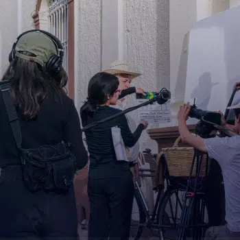 Equipo de rodaje en exterior con cámara, claqueta y micrófono de pértiga durante la grabación de una escena