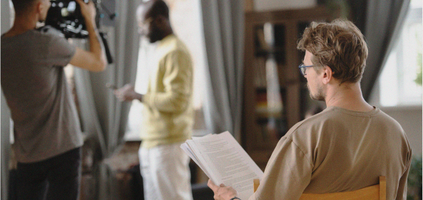 Una persona revisa un documento mientras otra graba a un actor al fondo