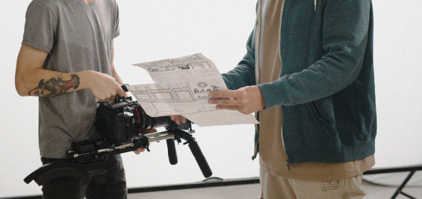 Dos personas revisan documentos. Una de ellas sostiene una cámara profesional