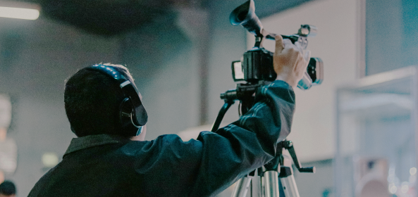 Operador de cámara con auriculares trabaja con una cámara sobre un trípode en un espacio cerrado