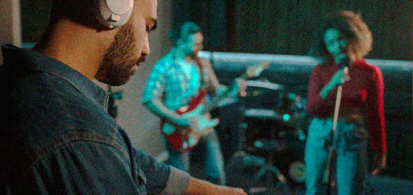 Técnico de sonido con auriculares grabando a una persona tocando la guitarra y a otra cantando