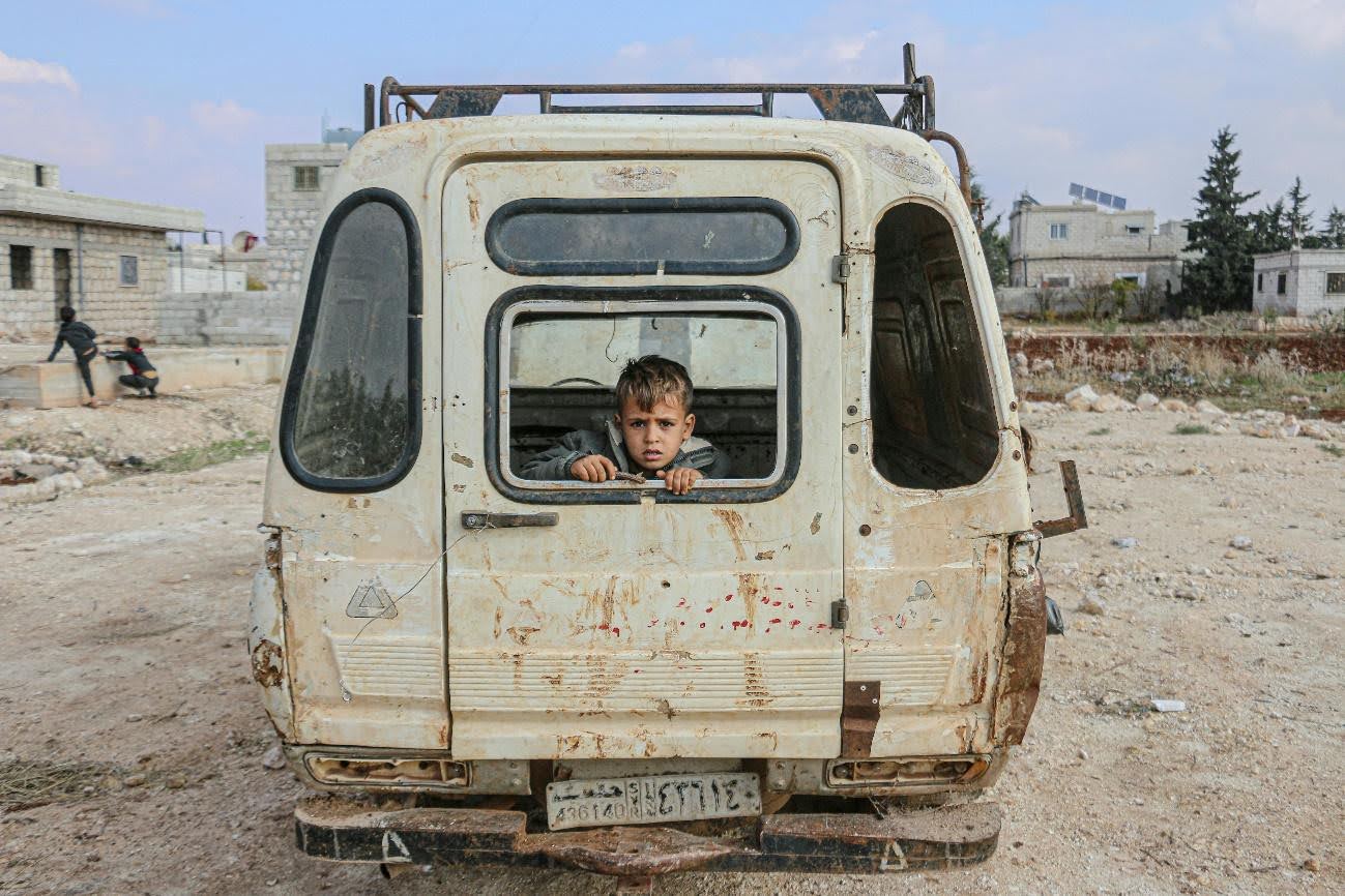 Fotograf&iacute;a de guerra de un ni&ntilde;o en una camioneta destruida en medio de un lugar desolado
