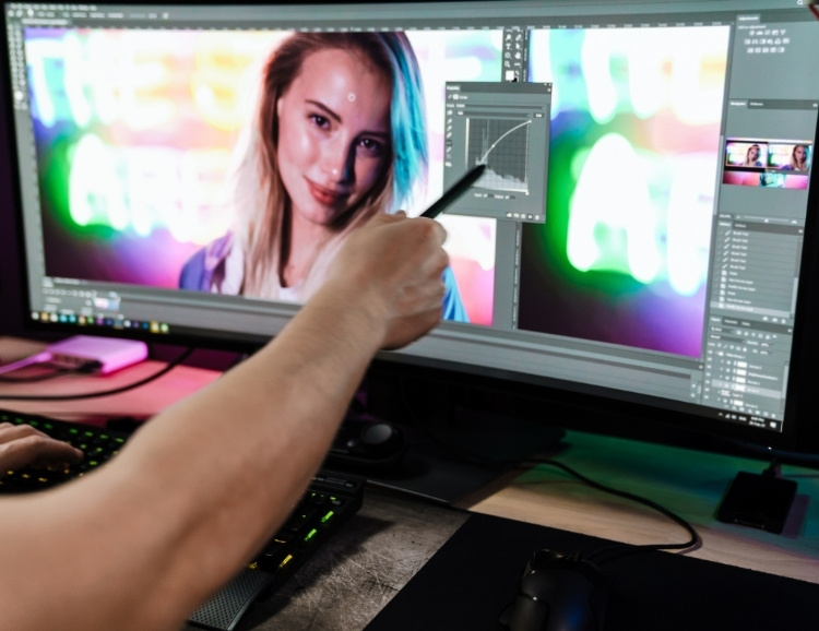 En la imagen, un hombre señala una pantalla en la que está editando la foto de una mujer para hacer un fotomontaje