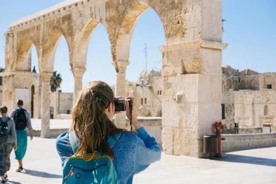 La imagen muestra a una joven de espaldas, sacándole una fotografía a un monumento