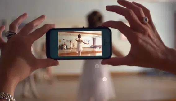 En la foto, una persona sostiene un smartphone para grabar el baile de una niña en una sala de danza