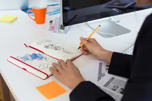 En la fotografía se ve a una mujer plasmando formas y colores en un sketchbook conceptual