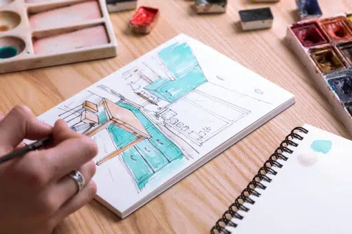 En la imagen, una mujer pinta una cocina en un sketchbook de práctica