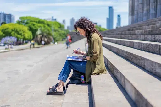 En la imagen, una mujer sentada en una escalera pública hace un dibujo de un paisaje